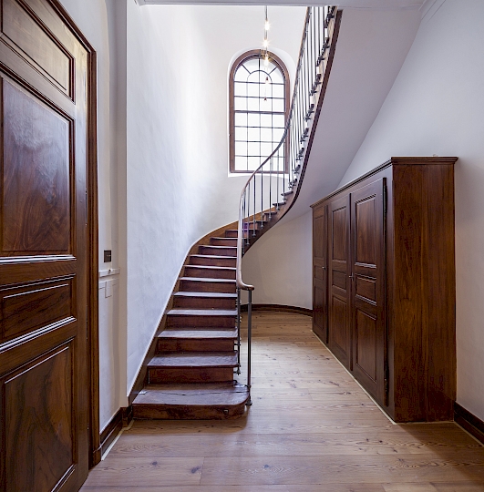 Vue générale des escaliers balancés donnant accès aux galeries de l’étage supérieur (nord-ouest). L’ancien plancher a été déposé et rem- placé par un parquet en mélèze brossé à l’ancienne (type Admonters). Des nouveaux luminaires ont été installés, un lustre Poulsen dans l’accès et une lampe sur mesure en inox dans la montée d’escaliers. Ponçage et huilage des marches en bois. Ponçage et peinture MLE4 du barreaudage. Confection d’une nouvelle armoire de rangement. Photo après travaux.